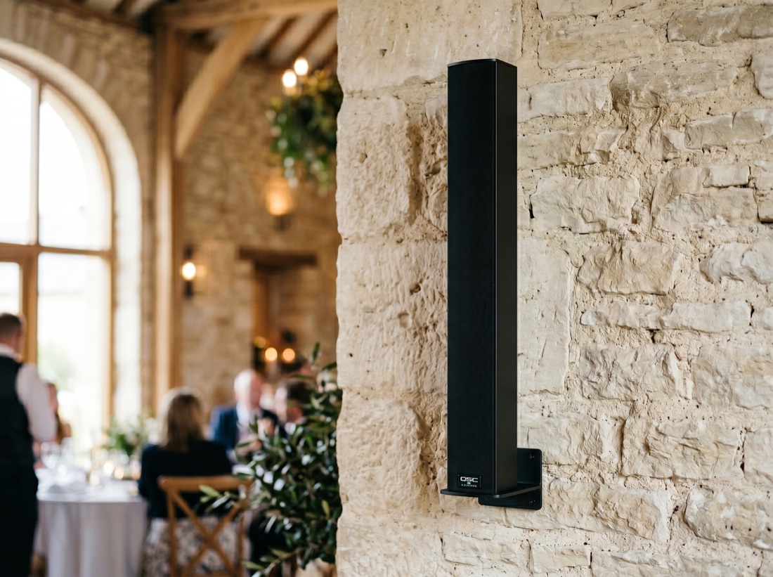 Enceinte colonne Wesound intégrée à un mur en pierre, salle de réception dressée en arrière-plan